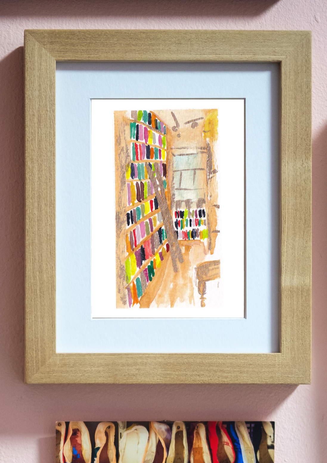 A framed art print featuring a colorful watercolor painting of a shop interior, displayed on a light pink wall above other framed pieces and a shoe rack.